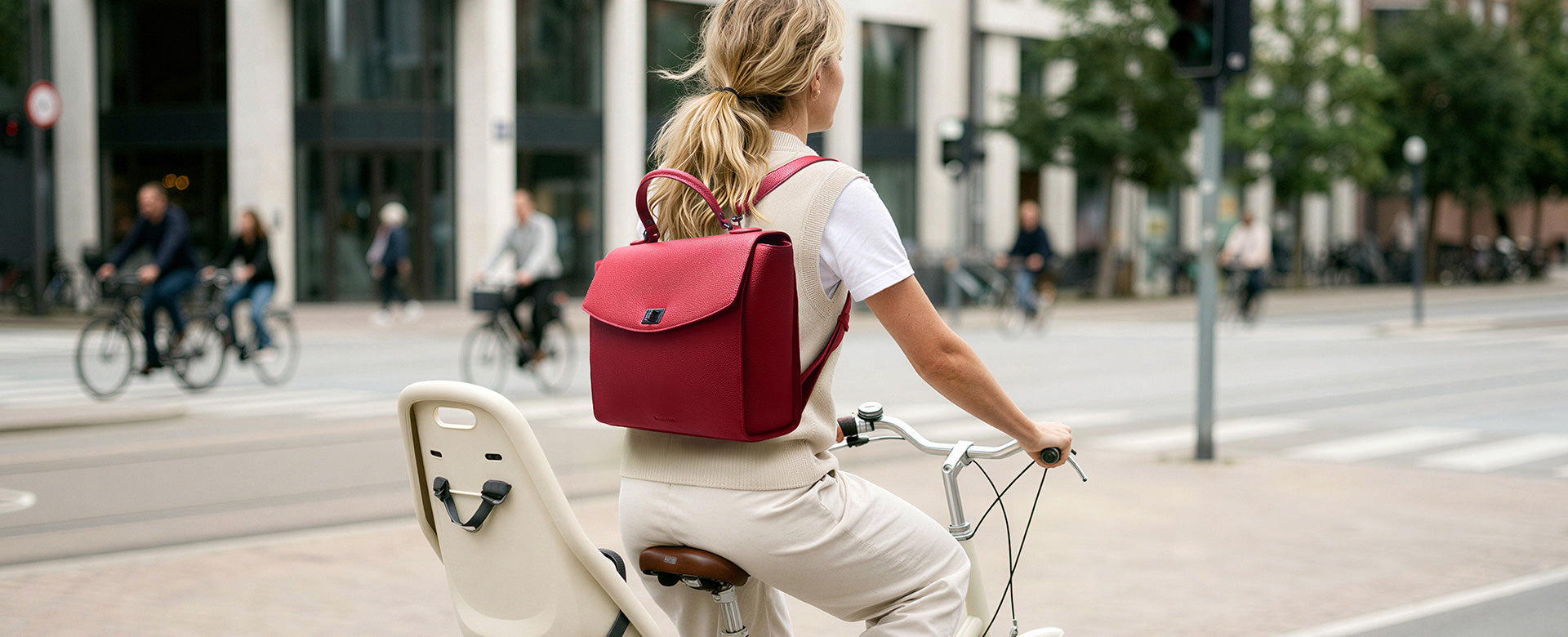 Geschäftlich gekleidete Frau beim Pendeln mit dem Fahrrad, ausgestattet mit einem eleganten roten Potter Rucksack.