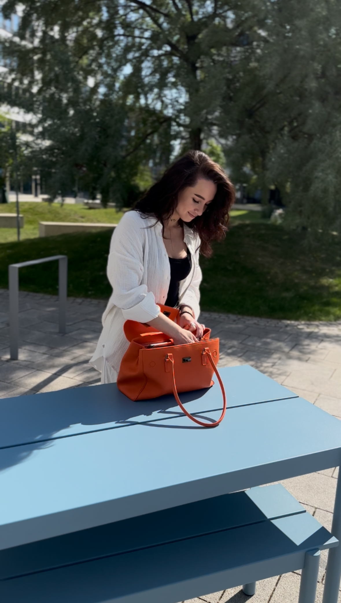 Frau organisiert ihre orangefarbene Victoria Hyde Business-Tasche im Freien auf modernem Tisch – nachhaltige Damenhandtasche, perfekt für Büro, Freizeit und Alltag, FAQ Bereich.