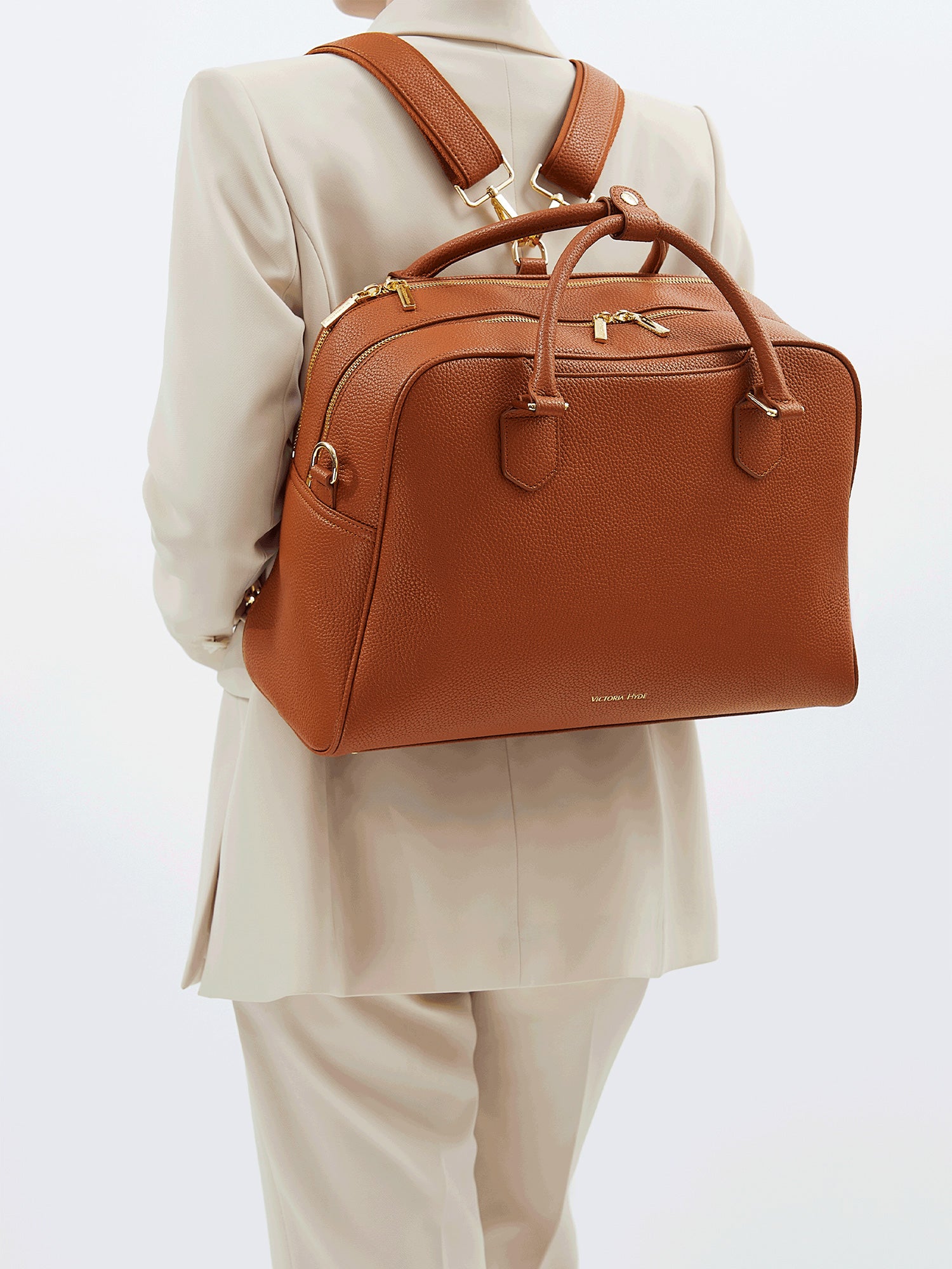 Model wearing Victoria Hyde Amal 2-in-1 brown laptop backpack, styled as a chic and ergonomic shoulder bag for professional commuters.