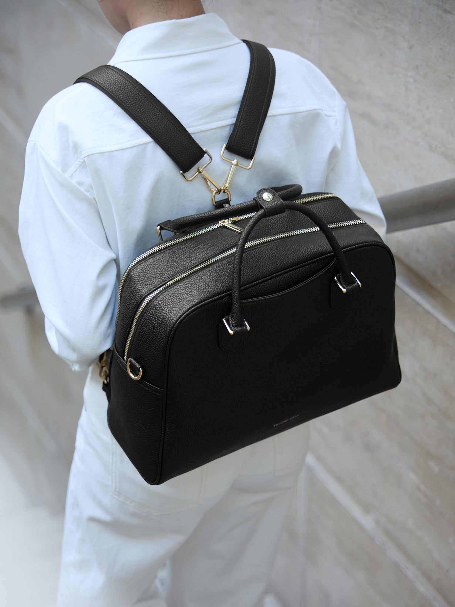 Model wearing Victoria Hyde Amal 3-in-1 black laptop backpack, styled as a chic and ergonomic shoulder bag for professional commuters.
