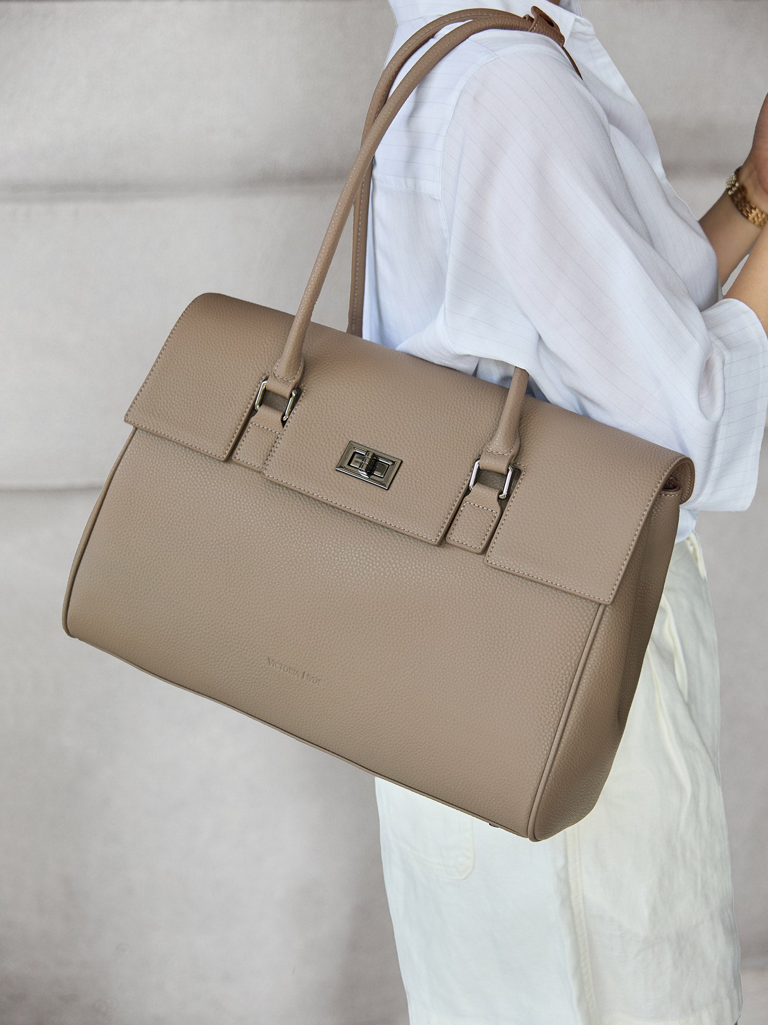 Model carrying the Victoria Hyde Jolene beige business laptop bag in brown as a shoulder bag, made of stylish, ergonomic vegan leather.