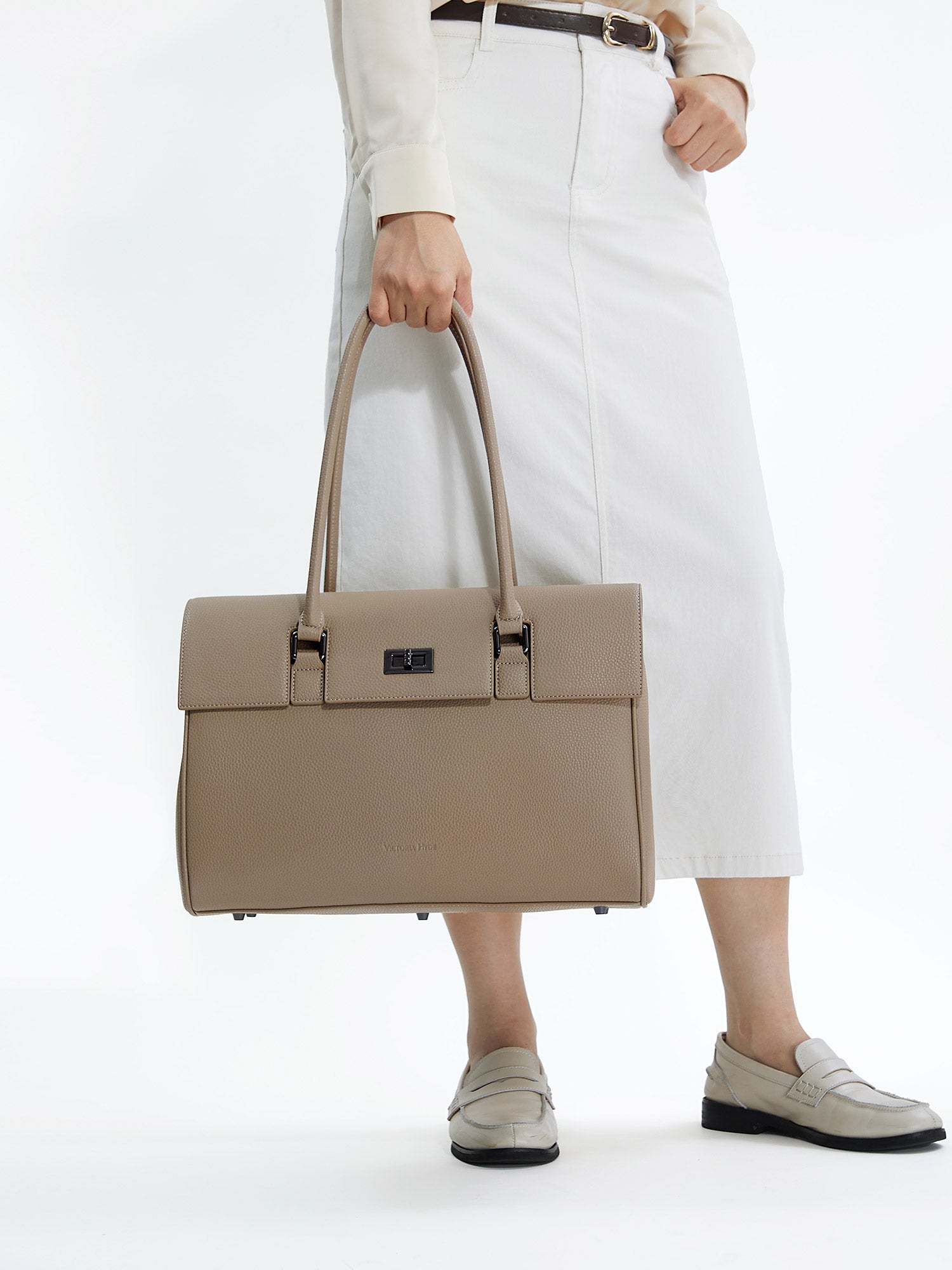 Professional woman carrying the Victoria Hyde Jolene beige laptop handbag, elegant vegan leather design with 15-inch laptop compartment for office work.