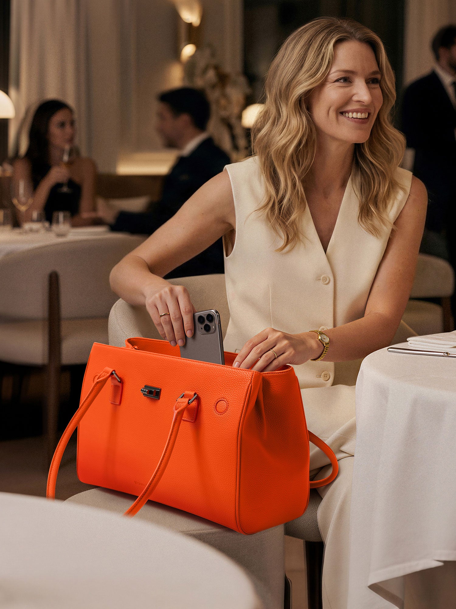 Woman in a restaurant using Victoria Hyde Jolene orange laptop bag, stylish vegan leather business tote for work and daily essentials.
