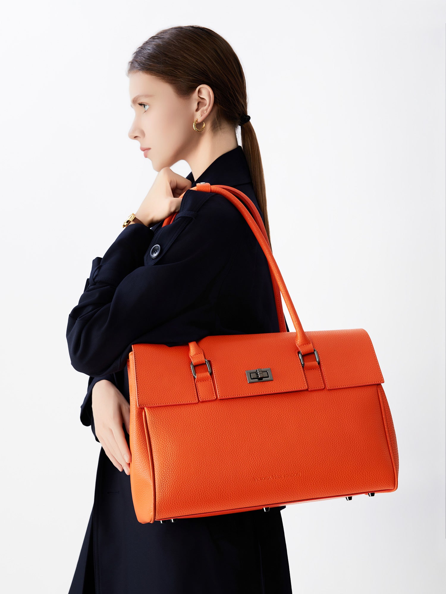 Model carrying the Victoria Hyde Jolene orange business laptop bag in brown as a shoulder bag, made of stylish, ergonomic vegan leather.