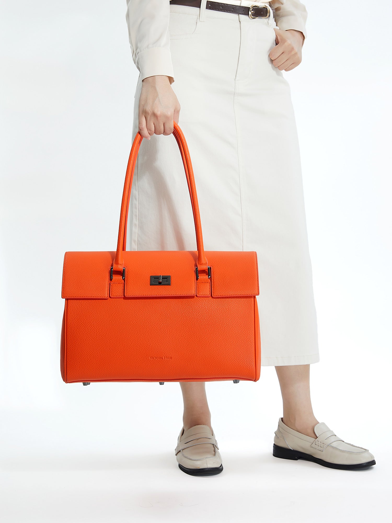 Professional woman carrying the Victoria Hyde Jolene orange laptop handbag, elegant vegan leather design with 16-inch laptop compartment for office work.