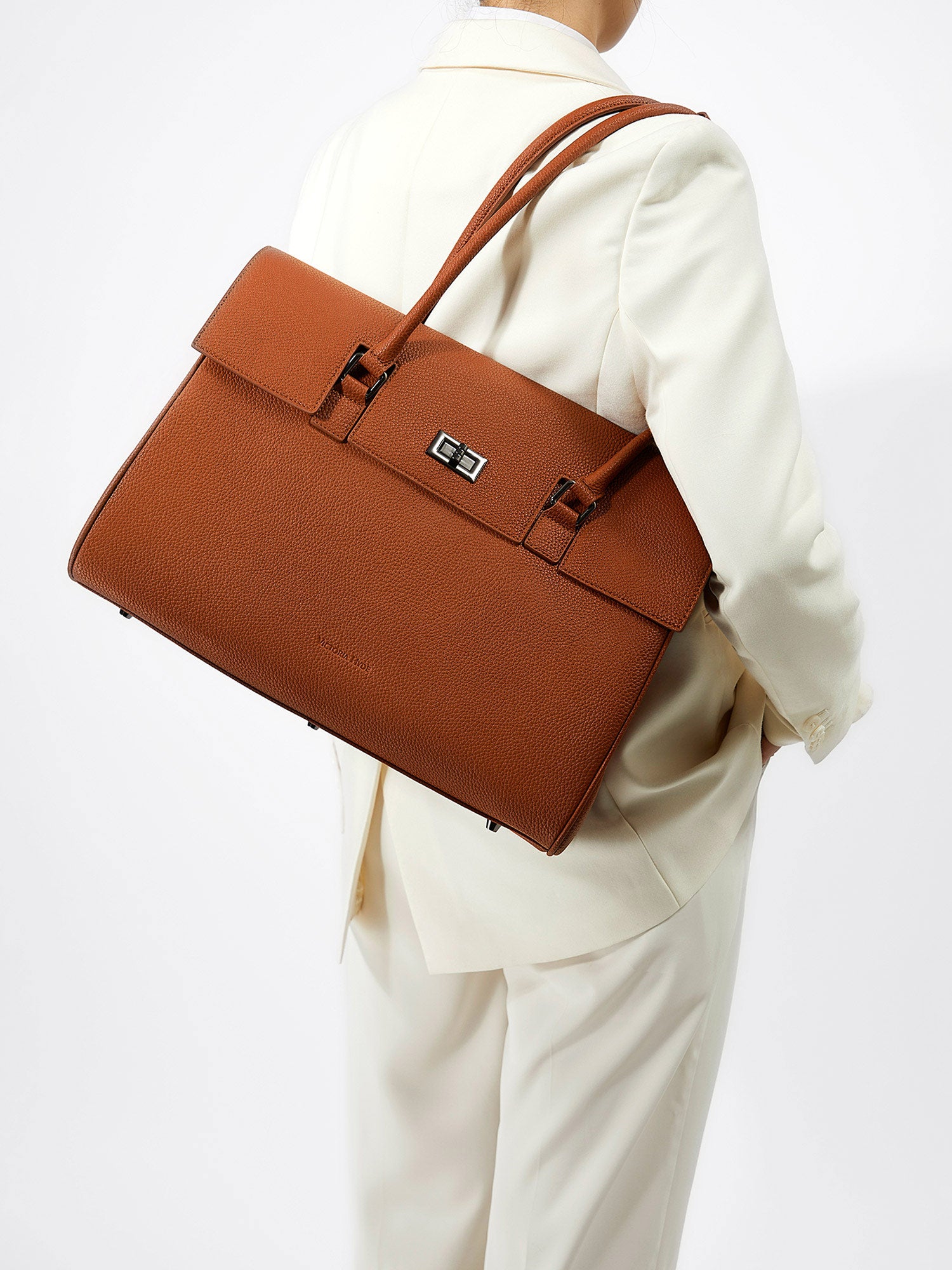 Model carrying the Victoria Hyde Jolene brown business laptop bag in brown as a shoulder bag, made of stylish, ergonomic vegan leather.