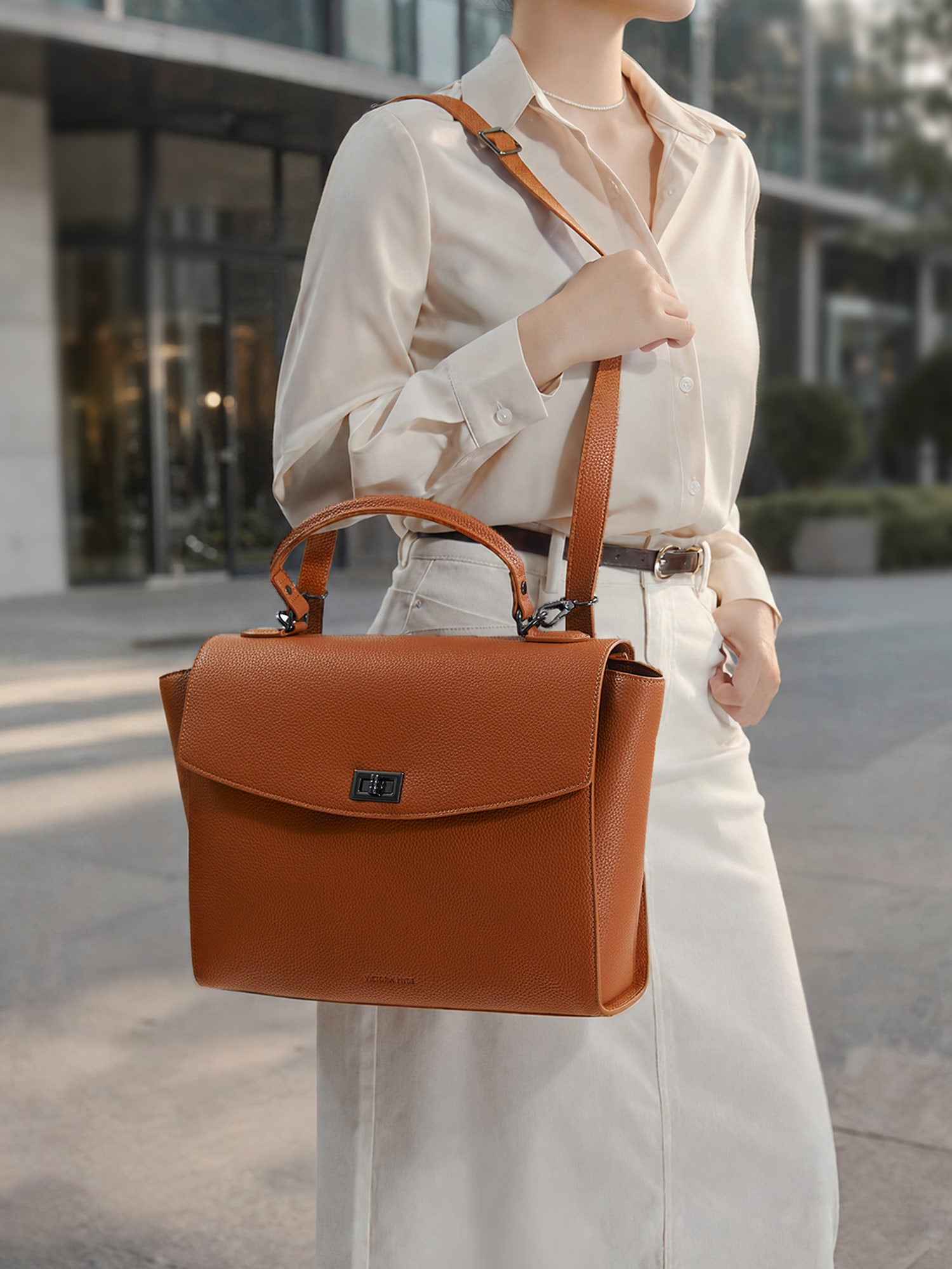 Model carrying the Victoria Hyde Potter 2-in-1 convertible laptop bag in braun as a shoulder bag, made of stylish, ergonomic vegan leather.