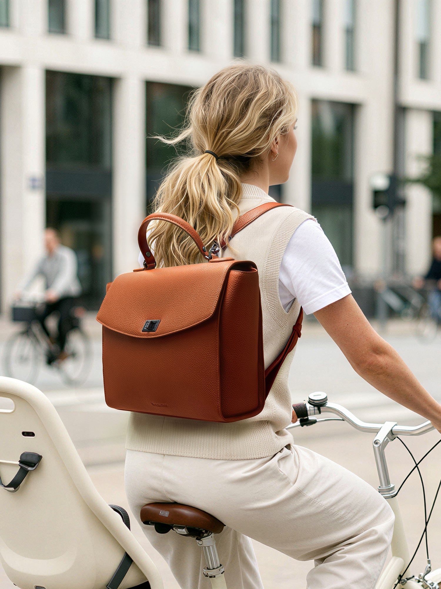 Woman cycling through the city wearing the Victoria Hyde Potter braun 2-in-1 convertible laptop backpack, showcasing its stylish vegan leather design for active professional commuters.