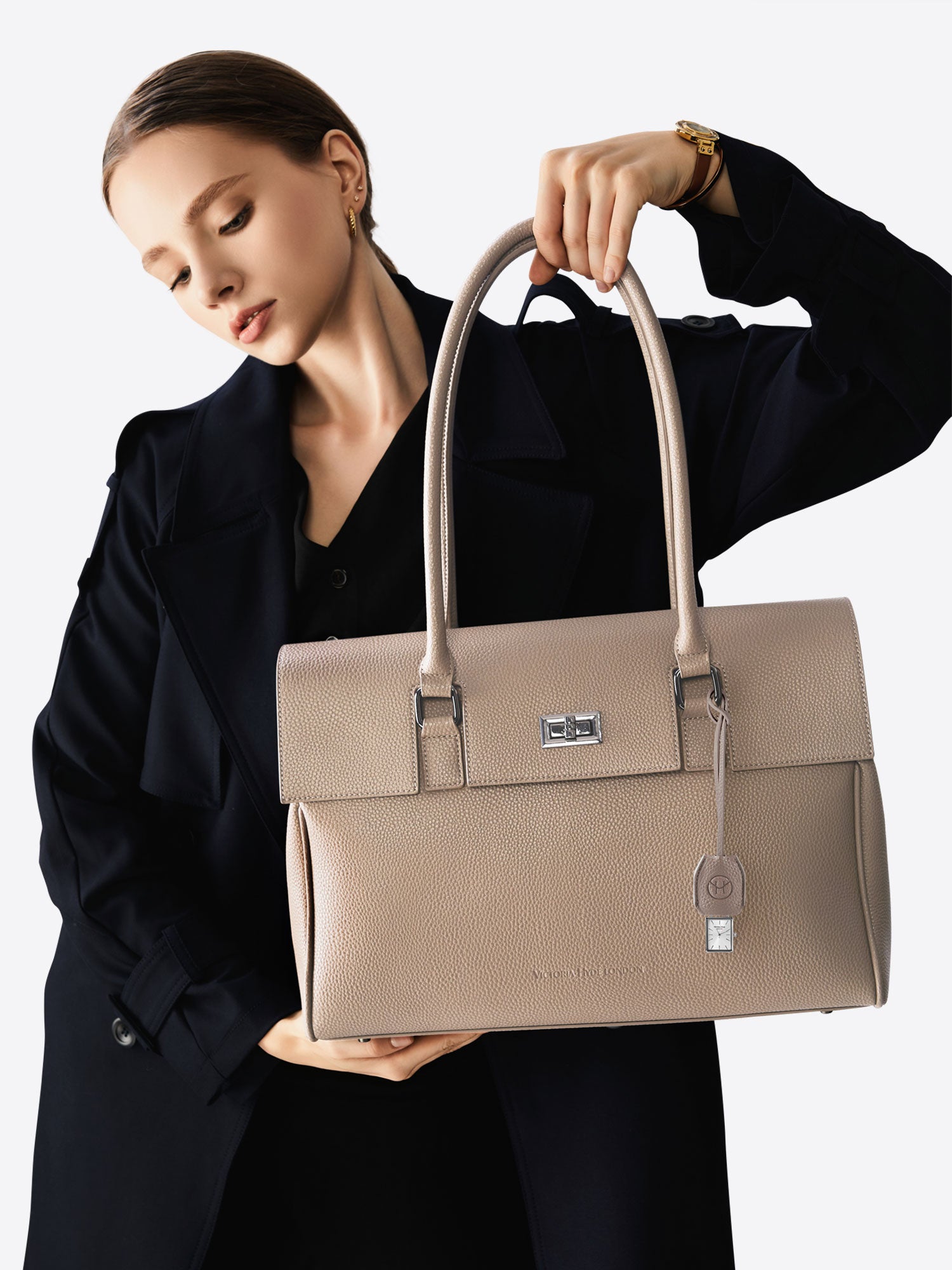 Victoria Hyde nude bag charm with watch and chain. Minimalist design with logo and flag symbol. Timeless accessory, 185mm chain length. Elegant functionality.