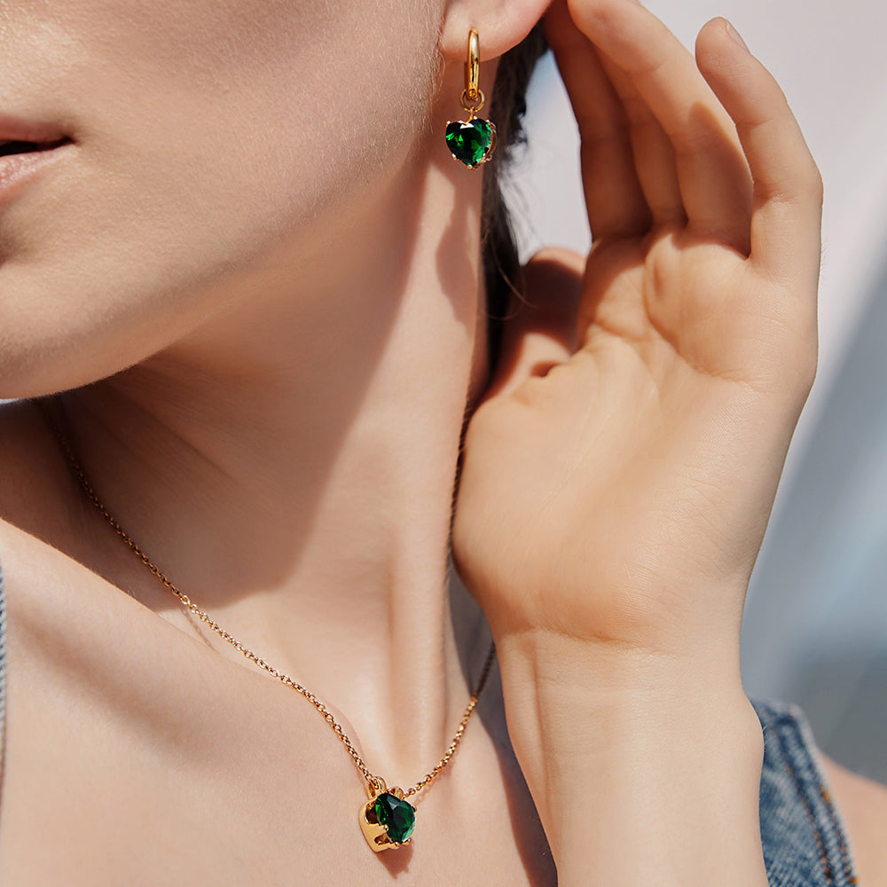 Victoria Hyde London heart-shaped jewelry set: necklace and earrings, light gold with deep green stones. Elegant, luxurious accessory for a refined look.