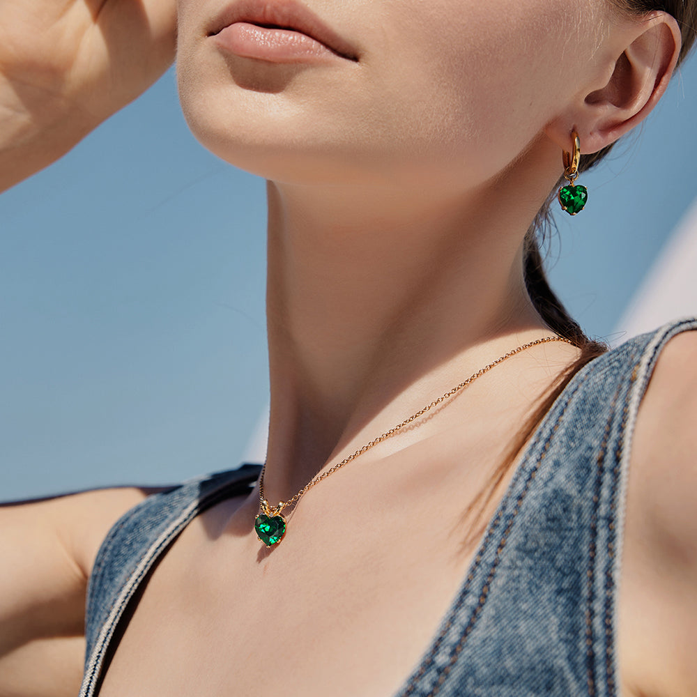 Victoria Hyde London heart-shaped jewelry set: necklace and earrings, light gold with deep green stones. Elegant, luxurious accessory for a refined look.