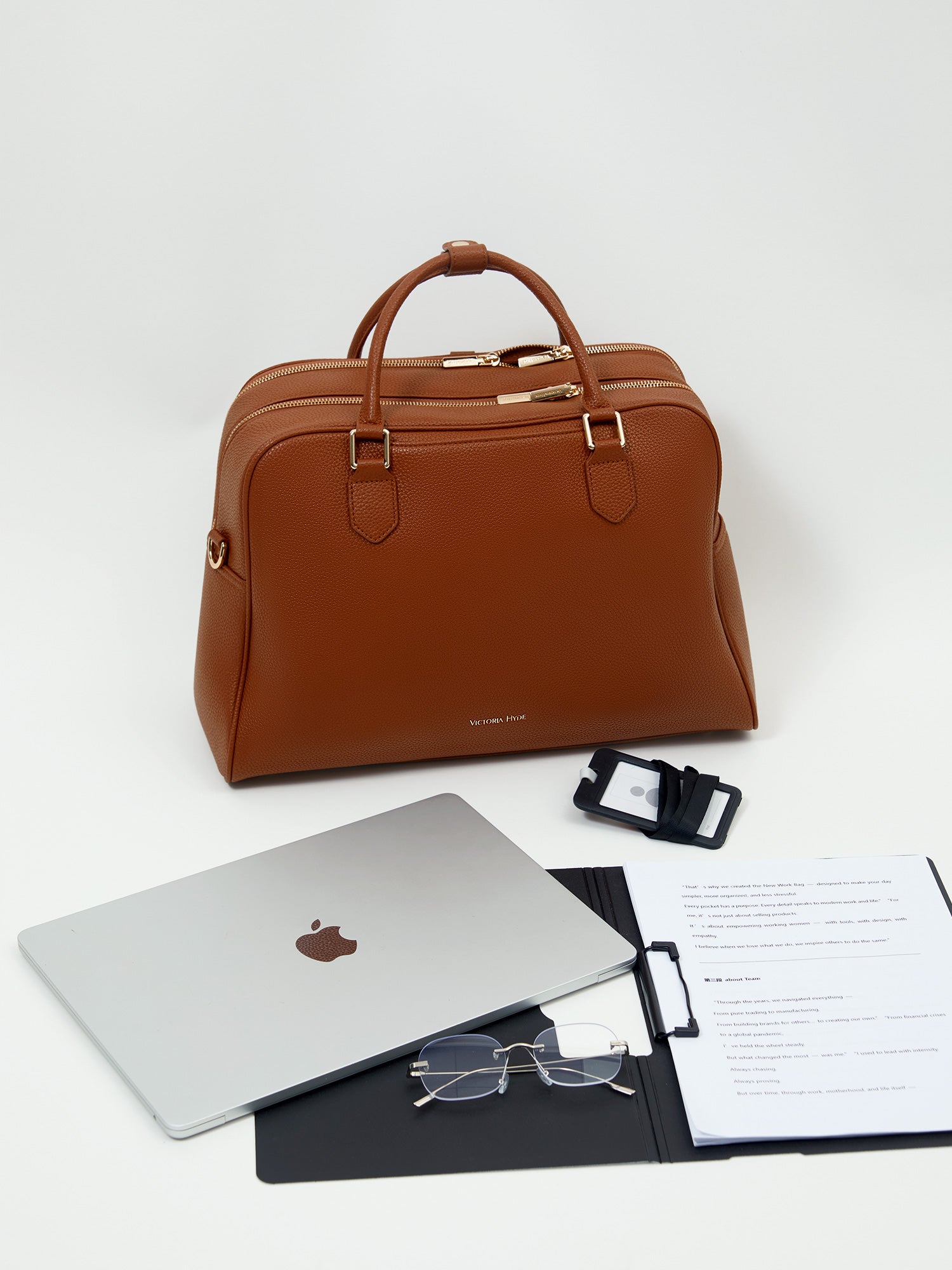 Victoria Hyde Amal 3-in-1 bag in brown vegan leather, styled as a chic handbag next to personal items, ideal for 14-inch laptops and professional commuters.