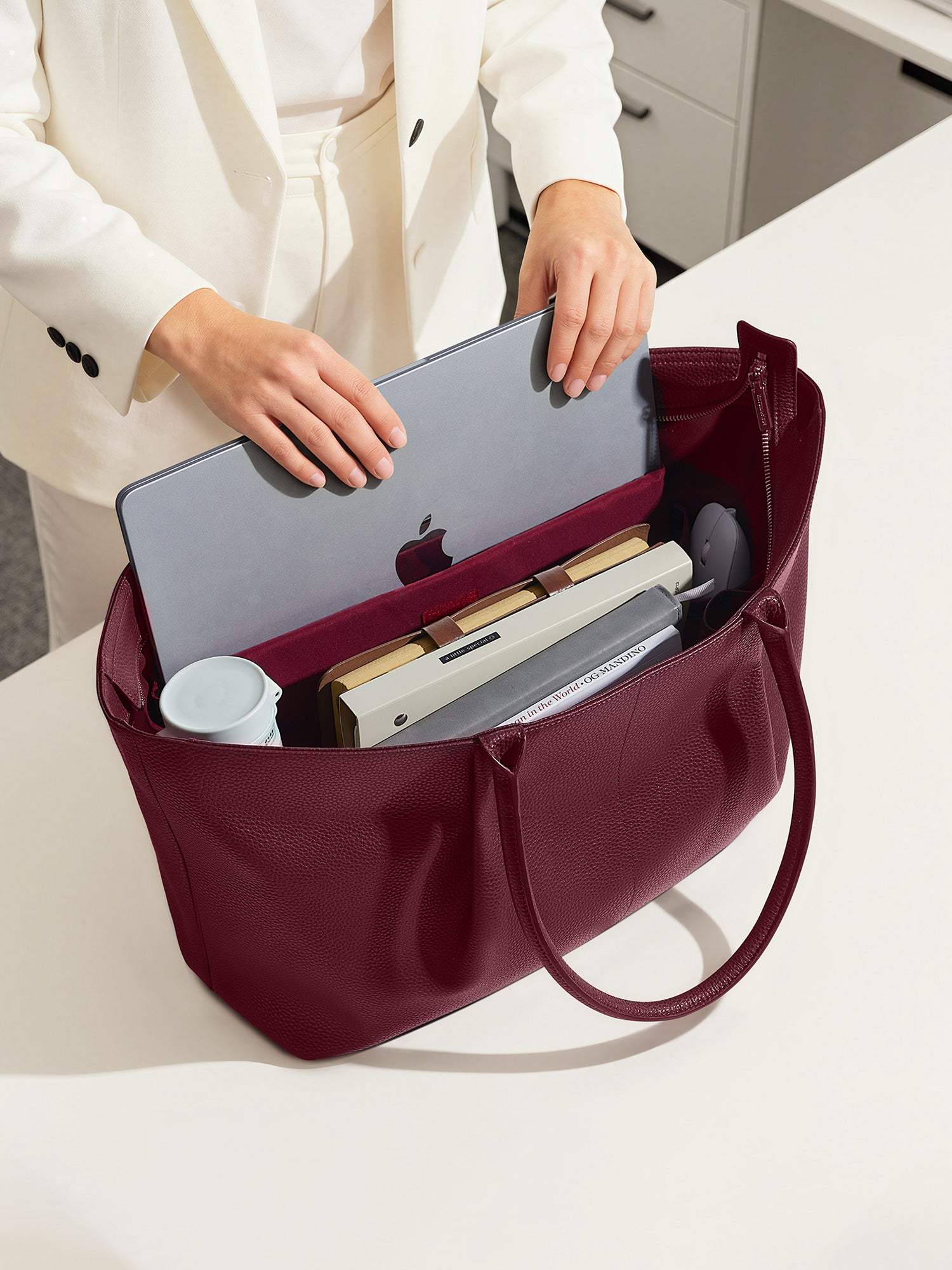Woman placing a 16-inch laptop into a Victoria Hyde Ada red business tote bag, highlighting the spacious, organized interior for professional office use.