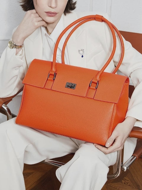 Victoria Hyde Jolene tote bag in orange vegan leather, styled as a chic handbag next to personal items, ideal for 16-inch laptops and professional commuters.