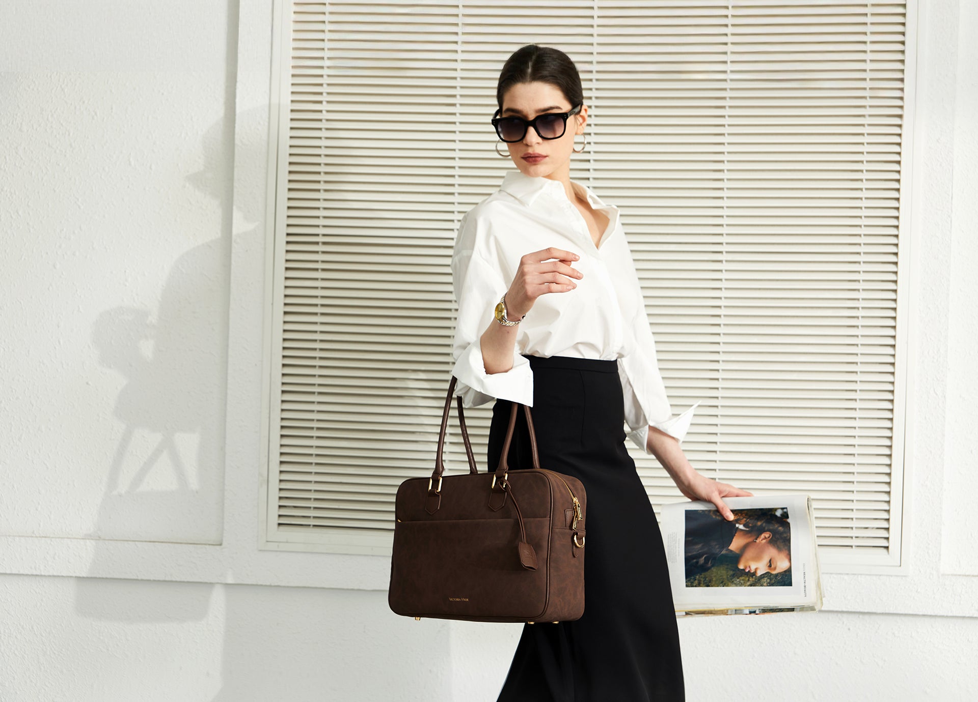 Eine Geschäftsfrau im weißen Hemd trägt die Victoria Hyde London Margaret Brown Business-Tasche. Diese funktionale und elegante braune Leder-Handtasche ist der perfekte Begleiter für den modernen "New Work"-Lifestyle und kombiniert berufliche Eleganz mit Alltagstauglichkeit für Frauen in Deutschland.