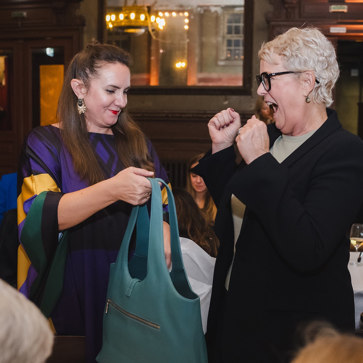 Begeisterte Teilnehmerinnen betrachten und präsentieren eine Victoria Hyde Shopper-Tasche auf dem STRIVE 100 Event am 17. Oktober 2025.